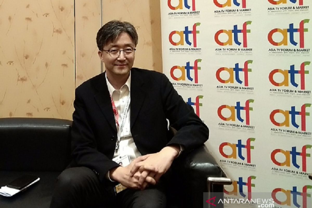  A man in a black suit is sitting on a couch in front of a backdrop with the words Asia TV Forum & Market.