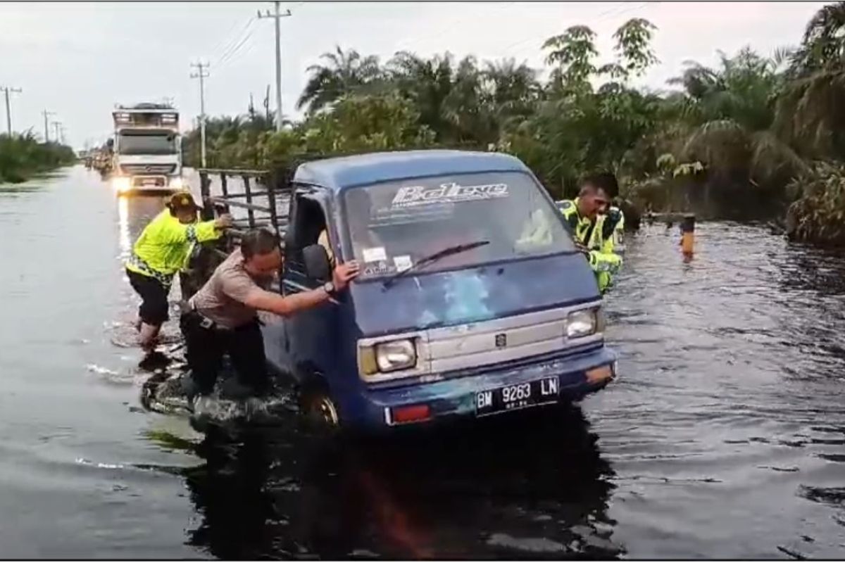 Anggota Polres Pelalawan bantu pengendara lewati banjir sambil serukan pemilu damai