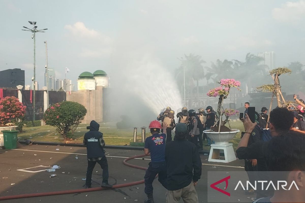 Massa lempari polisi dengan batu saat petugas coba padamkan api  di depan gedung DPR RI