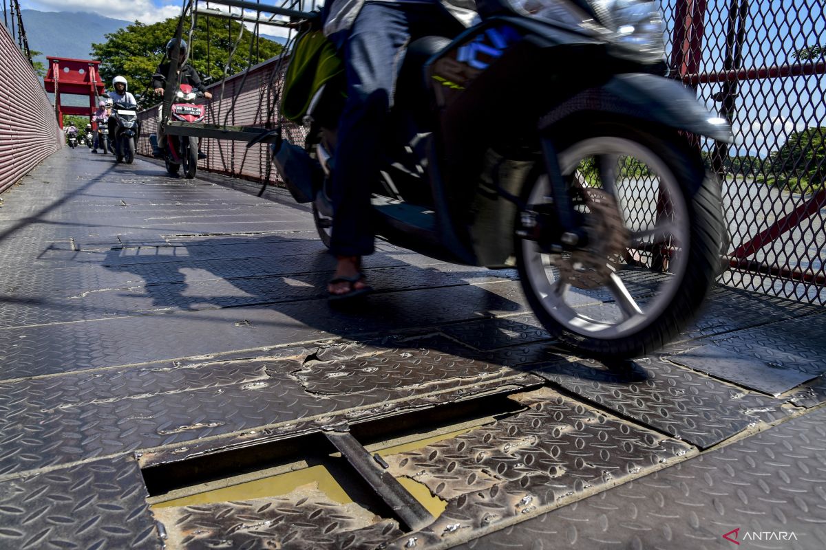 Pengendara roda dua melintas dekat plat besi jembatan gantung