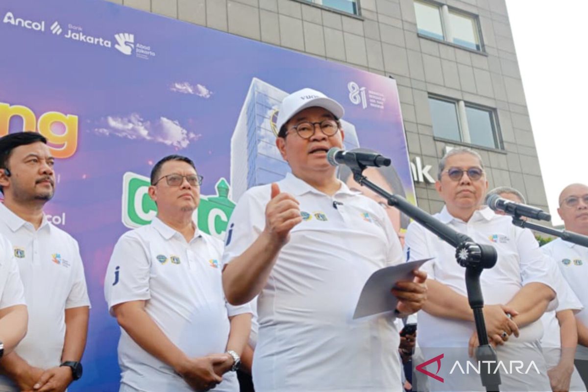Seorang pejabat berbicara di depan mikrofon dengan latar belakang banner ungu bertuliskan "Ancol in Jakarta" di sebuah acara resmi di Jakarta.
