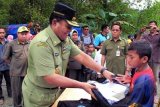 Gubernur Maluku Karel Albert Ralahalu (kiri) menyerahkan pakaian seragam dan peralatan sekolah kepada anak korban bencana jebolnya Natural Dam Way Ela, di Desa Negeri Lima, Pulau Ambon, Maluku Tengah, Maluku, Senin (12/8). Sebanyak 439 siswa SD, 285 siswa SMA, 321 siswa SMP, 25 siswa Taman Pengajian dan 58 siswa Paud yang menjadi korban bencana alam tersebut memperoleh seragam dan peralatan sekolah baru bantuan Pemprov Maluku dan Badan Nasional Penanggulangan Bencana (BNPB), serta membangun 13 tenda sebagai sekolah darurat dan proses belajarnya mulai berjalan 15 Agustus. ANTARA FOTO/Jimmy Ayal/ss/mes/13.