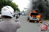 Seorang petugas polisi memotret mobil terbakar dengan kamera telepon genggamnya sebelum mengosongkan lokasi kejadian di Pekanbaru, Jumat (20/12). Mobil jenis minibus milik warga itu terbakar tak jauh dari Mapolda Riau, yang diduga terjadi akibat arus pendek listrik. ANTARA FOTO/FB Anggoro/nym/2013.