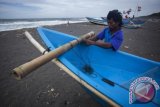 Seorang nelayan memperbaiki kapalnya di Pantai Samas, Bantul, Yogyakarta, Selasa (21/1). Hampir satu minggu nelayan di pantai selatan Yogyakarta tersebut tidak berani melaut karena gelombang tinggi yang menurut BMKG sebesar 3 hingga 5 meter akibat adanya daerah pusat tekanan rendah (low pressure) di utara dan barat Australia serta dipengaruhi oleh siklon tropis June yang terjadi di Samudra Pasifik. ANTARA FOTO/Sigid Kurniawan/wra/14