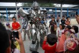 Sejumlah anak dan orang dewasa menyaksikan aksi salah satu tokoh robot dalam film Transformers, Megatron, yang sedang mengamen di pelataran Stasiun Depok Baru, Jabar, Jum'at (8/8). Robot Megatron yang bisa mengeluarkan suara khas dan berjoget itu dikenakan oleh sang seniman pembuat kostum Cosplay, Fiki Fadilah untuk mengamen dan menjadi daya tarik tersendiri bagi anak-anak hingga orang dewasa yang menyaksikan. ANTARA FOTO/Indrianto Eko Suwarso/ed/pd/14