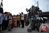 Sejumlah anak dan orang dewasa menyaksikan aksi salah satu tokoh robot dalam film Transformers, Megatron, yang sedang mengamen di pelataran Stasiun Depok Baru, Jabar, Jum'at (8/8). Robot Megatron yang bisa mengeluarkan suara khas dan berjoget itu dikenakan oleh sang seniman pembuat kostum Cosplay, Fiki Fadilah untuk mengamen dan menjadi daya tarik tersendiri bagi anak-anak hingga orang dewasa yang menyaksikan. ANTARA FOTO/Indrianto Eko Suwarso/ed/pd/14