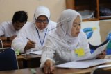 Seorang peserta Ujian Nasional Paket C berumur 61 tahun, Romdoniah (tengah) mengerjakan soal mata pelajaran Sosiologi di SMPN 2 Depok, Jawa Barat, Selasa (14/4). Nenek 4 anak dan 8 cucu pemilik sekolah PAUD Aulia di Serua, Bojong Sari tersebut jika lulus berencana melanjutkan ke perguruan tinggi. ANTARA FOTO/Indrianto Eko Suwarso/ss/Spt/15