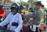 Polisi mengenakan helm standar SNI kepada pengendara sepeda motor saat Operasi Simpatik di kawasan Jalan Sudirman, Kota Denpasar, Bali, Senin (20/4). Pembagian helm tersebut sebagai bentuk sosialisasi kesadaran keselamatan lalu lintas dengan menggunakan peralatan yang standar dan lengkap. ANTARA FOTO/Fikri Yusuf/wdy/15.