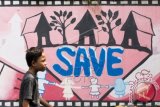 Seorang anak melintas dekat graffiti 'save anak' di Jakarta, Minggu (28/6). Komisi Perlindungan Anak Indonesia (KPAI) menyatakan kekerasan pada anak tiap tahunnya mengalami peningkatan dari tahun 2011 terjadi sebanyak 2178, 2012 ada 3512 kasus, 2013 ada 4311 kasus dan tahun 2014 ada 5066 kasus. ANTARA FOTO/M Agung Rajasa/wdy/15.