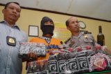 Polisi menunjukkan barang bukti kasus pembuatan dan pengedaran obat tanpa izin edar di depan tersangka, Saifudin (berpenutup wajah) di Mapolres Madiun, Jawa Timur, Jumat (28/8). Polisi memeriksa dan menahan Saifudin tersangka pembuat dan pengedar obat racikan untuk sakit asam urat tanpa memiliki izin produksi dan izin edar. Antara Jatim/Foto/Siswowidodo/15