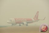 Sebuah pesawat milik maskapai penerbangan Air Asia berada di landasan Bandara Supadio yang diselimuti kabut asap di Kubu Raya, Kalbar, Rabu (21/10). Aktivitas penerbangan domestik dan internasional di Bandara Supadio kembali terganggu asap pekat, hingga mengakibatkan jarak pandang berada di bawah 700 meter dan tidak aman bagi penerbangan. ANTARA FOTO/Jessica Helena Wuysang/15