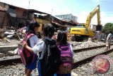 Tiga siswa melihat alat berat merobohkan bangunan di pinggir rel kawasan AR Hakim - Mandala, di Medan, Sumatera Utara, Kamis (21/1). Kawasan bangunan yang dirobohkan tersebut, akan dibangun jalur ganda (double track) kereta api Bandara Kualanamu. ANTARA SUMUT/Irsan Mulyadi/16