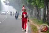 Pensiunan anggota Satuan Polisi Pamong Praja Pemerintah Kota Pontianak, Sailam (68 tahun) berjalan kaki dengan membawa bendera di Jalan Arteri Supadio, Kabupaten Kubu Raya, Kalbar, Rabu (17/8). Setiap tahun Sailam merayakan hari ulang tahunnya yang bertepatan dengan HUT Kemerdekaan RI, dengan berjalan kaki sambil membawa bendera merah putih dari kediamannya di Kota Pontianak menuju Bandara Supadio sejauh 20 Kilometer pulang pergi (PP). ANTARA FOTO/Jessica Helena Wuysang/16