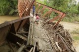 Warga melintasi jembatan yang rusak pascabanjir luapan Sungai Bugha di Desa Bugha, Kecamatan Seulimum, Kabupaten Aceh Besar, Aceh, Senin (2/1). Banjir yang disebabkan guyuran hujan selama beberapa jam pada Senin (2/1) dini hari mengakibatkan jembatan rusak sehingga mengganggu transportasi antardesa, dan juga merusak ratusan hektar tanaman pisang dan padi milik warga. ANTARA FOTO/Ampelsa/kye/17