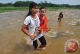 Seorang wanita saat menggendong putrinya yang akan mengikuti perayaan Hari Kartini tahun 2017 menyeberangi Sungai Blukar di Dusun Cipluk, Sidokumpul, Patean, Kendal, Jawa Tengah. Meski harus menerjang arus sungai yang cukup deras karena tidak tersedianya jembatan, puluhan pelajar di dusun itu tetap bersemangat berangkat sekolah untuk mengikuti upacara peringatan Hari Kartini. (ANTARA FOTO/Anis Efizudin/Dok).