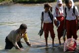 Bhabinkamtibmas Desa Mongiilo Utara Aipda Ismet Ishak (kiri) membantu siswa yang menaiki rakit penyeberangan untuk berangkat ke Sekolah Dasar (SD) Negeri 1 Bulango Ulu, Kabupaten Bone Bolango, Gorontalo, Selasa (5/9). Sebanyak 30 siswa dari Mongiilo Utara dan Ilomata harus berjalan kaki sejauh 2-4 kilometer dari rumah mereka dan menyeberangi sungai untuk berangkat ke sekolah yang berada di Mongiilo Induk. (ANTARA FOTO/Adiwinata Solihin).