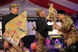 Gubernur Jawa Timur Soekarwo (kanan) menyerahkan wayang kulit kepada dalang Ki Manteb Soedharsono (tengah) didampingi dalang Ki Anom Suroto (kiri) saat Festival Wayang Kulit di Surabaya, Jawa Timur, Selasa (17/10). Pagelaran wayang kulit dengan dalang Ki Manteb Soedharsono dengan Ki Anom Suroto berlakon 'Lamabad Wonomarto' itu dalam rangka Hari Jadi Ke-72 Provinsi Jawa Timur. Antara Jatim/Didik Suhartono/uma/17