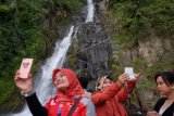 Wisatawan berfoto dengan latar belakang Air Terjun Binangalom, Danau Toba, Toba Samosir, Sumatera Utara, Jumat (27/10). Air terjun yang jatuh langsung ke Danau Toba tersebut merupakan salah satu objek wisata yang banyak dikunjungi wisatawan. ANTARA FOTO/Irsan Mulyadi/ama/17.