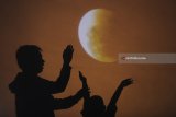 Warga berpose dengan latar gerhana bulan 'super blue blood moon' yang ditampilkan di layar saat gerhana tersebut terlihat dari Masjid Al-Akbar, Surabaya, Jawa Timur, Rabu (31/1). Antara Jatim/Zabur Karuru/zk/18