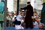 Terpidana (duduk) pelanggar peraturan daerah (qanun) tentang syariat islam menjalani eksekusi hukuman cambuk di hadapan warga di halaman Masjid Jami' Kemukiman Lueng Bata, Banda Aceh, Aceh, Jumat (20/4/2018). Mahkamah Syar'iah menjatuhkan hukuman sebanyak 12 hingga 22 kali cambuk di muka umum kepada delapan terpidana pelanggar Qanun Aceh nomor 6/2014 tentang hukum Jinayat. (ANTARA /Irwansyah Putra) 