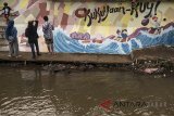 Sejumlah mahasiswa melukis mural Cau Pisun di kirmir (tebing sungai) Sungai Cikapundung kawasan Linggawastu, Bandung, Jawa Barat, Minggu (15/4). Mural yang dilukis mahasiswa TPB FSRD Seni Rupa ITB tersebut untuk mengembalikan fungsi kampung kreatif yang bercerita tentang aktivitas dan kepekaan warga lokal dalam menjaga kebersihan dan ekosistem sungai Cikapundung. ANTARA JABAR/Novrian Arbi/agr/18