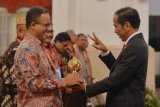 Presiden Joko Widodo (kanan) menyerahkan penghargaan Jaminan Kesehatan Nasional-Kartu Indonesia Sehat (JKN-KIS) Award kepada Gubernur DKI Jakarta Anies Baswedan ketika menerima pengguna manfaat kartu tersebut di Istana Negara, Jakarta, Rabu (23/5/2018). Sebanyak empat provinsi menerima penghargaan JKN-KIS Award terkait perlindungan kesehatan terbaik di rumah sakit dengan persentase hingga 95 persen, selain itu juga terdapat kepala daerah dari 28 kota dan 92 kabupaten menerima award tersebut. (ANTARA /Wahyu Putro A) 