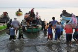 Buruh angkut menggendong pemudik sebelum menaiki perahu nambangan atau perahu penghubung dari darat ke Perahu Layar Motor di Pelabuhan Jangkar, Situbondo, Jawa Timur, Sabtu (9/6). Selama musim mudik buruh angkut pendapatannya naik dari Rp25.000 menjadi Rp70.000 per hari dengan mengangkut orang, barang dan sepeda motor pemudik dari pinggir pantai ke perahu nambangan. Antara Jatim/Seno/zk/18.