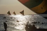 Pengunjung bermain perahu layar di Pantai Pasir Putih Situbondo, Jawa Timur, Minggu (17/6). Masyarakat memanfaatkan libur Lebaran dengan menikmati matahari terbenam, berenang di laut, naik perahu layar dan bermain kano.
 Antara Jatim/Seno/zk/18.