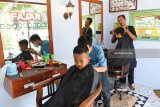 Siswandi memotong rambut pelanggannya di Kelurahan Banjarsari, Glagah, Banyuwangi, Jawa Timur, Selasa (12/6). Siswandi merupakan warga yang berprofesi sebagai tukang potong rambut yang menyambi sebagai relawan penjaga perlintasan kereta api di Banjarsari, yang volume pemotongan rambutnya meningkat dari 10 orang menjadi 25 orang per hari menjelang Lebaran 2018 dengan biaya potong Rp 10.000 per orang. Antara Jatim/Seno/zk/18.