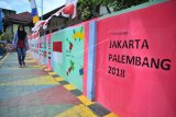 Warga melintasi salah satu bagian kampung yang telah dihiasi dengan warna warni logo Asian Games di Kampung Cempaka Bukit Kecil Palembang,sumsel, Minggu (24/6). Untuk mensosialisasikan Asian Games kawasan perkampungan di Kota Palembang berlomba mempercantik diri dengan aneka warna dan logo Asian Games. ANTARA FOTO/Feny Selly/pd/18