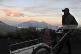 Penambang belerang mendorong gerobak atau troli dengan latar belakang Gunung Raung di Gunung Ijen, Banyuwangi, Jawa Timur, Minggu (22/7). Kawah Gunung Ijen menjadi daya tarik bagi wisatawan nusantara dan mancanegara karena memeliki kawah seluas sekitar 5.466 hektar, bisa melihat api berwarna biru (blue fire), matahari terbit, dan terdapat taksi manusia atau ojek manusia. Antara Jatim/Seno/zk/18.