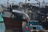 Petugas berusaha melakukan upaya pemadaman dan pendinginan kapal ikan yang terbakar di Pelabuhan Benoa, Denpasar, Bali, Rabu (11/7). Petugas terus melakukan penyemprotan air untuk memadamkan dan mendinginkan bagian sejumlah kapal dari total 40 unit kapal yang terbakar sejak Senin (9/7) tersebut. ANTARA FOTO/Fikri Yusuf/wdy/2018