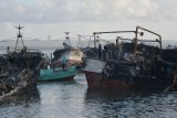 Warga mengamati puing-puing kapal ikan yang terbakar di Pelabuhan Benoa, Denpasar, Bali, Selasa (10/7). Puing-puing sisa peristiwa kebakaran 40 unit kapal yang menimbulkan kerugian sekitar Rp120 miliar itu rencananya akan segera digeser dari sekitar dermaga agar tidak mengangggu aktivitas lalu lintas kapal nelayan di pelabuhan tersebut. ANTARA FOTO/Fikri Yusuf/foc/18.