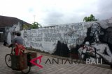 Pedagang melintas di samping karya seni mural menolak PLTU Celukanbawang di kawasan Jalan Ratna, Denpasar, Kamis (30/8). Seni mural tersebut digagas oleh 10 orang seniman Komunitas Pojok dan Greenpeace dengan mengambil tema 'Mural Jamming' sebagai bentuk penolakan terhadap PLTU Batubara di Celukanbawang, Kabupaten Buleleng. ANTARA FOTO/Wira Suryantala/wdy/2018.