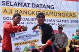 Peraih medali emas cabang olahraga pencak silat Asian Games 2018 asal Ponorogo, Aji Bangkit Pamungkas (kiri) menerima secara simbolis bonus uang Rp100 juta dari Pemkab Ponorogo yang diserahkan Bupati Ponorogo Ipong Muchlissoni (kedua kiri) saat acara penyambutan di Ponorogo, Jawa Timur, Kamis (6/9). Kedatangan Aji Bangkit Pamungkas di daerah kelahiran disambut puluhan ribu orang saat pawai sejauh sekitar 10 kilometer sebagai bentuk penyambutan dan apresiasi. Antara Jatim/Siswowidodo/mas/18.