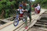 Prajurit TNI membantu siswa melintasi jembatan darurat saat perbaikan bersama warga dalam program TNI manunggal membangun desa TMMD di desa Ujong Raja, Panton Reu, Aceh Barat, Aceh (24/10) (Antara Aceh/Syifa Yulinnas)