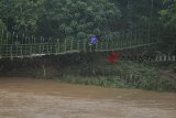 Warga melintasi jembatan gantung di Desa Cipatujah, Kabupaten Tasikmalaya, Jawa Barat, Rabu (7/11/2018). Akibat jembatan Pesangrahan Cipatujah tidak bisa dilalui akibat diterjang banjir bandang, sebagian warga terpaksa melewati jembatan gantung alternatif yang menghubungkan Desa Cipatujah dengan Desa Ciandum untuk beraktivitas meskipun jembatan tersebut tidak layak dilewati. ANTARA JABAR/Adeng Bustomi/agr.