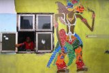 Seorang ibu membuka jendela disamping mural tokoh wayang kulit Prabu Baladewa di Kampung Wayang Kulit, Pisangcandi, Malang, Jawa Timur, Kamis (22/11).Warga di kampung tersebut sengaja menghiasi tembok rumahnya dengan 50 karakter tokoh wayang kulit sebagai upaya edukasi dan pelestarian budaya. Antara Jatim/Ari Bowo Sucipto/ZK. 