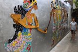 Seorang ibu melintas di depan mural tokoh wayang kulit keluarga Arjuna di Kampung Wayang Kulit, Pisangcandi, Malang, Jawa Timur, Kamis (22/11).Warga di kampung tersebut sengaja menghiasi tembok rumahnya dengan 50 karakter tokoh wayang kulit sebagai upaya edukasi dan pelestarian budaya. Antara Jatim/Ari Bowo Sucipto/ZK. 