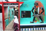 Seorang ibu melintas di depan mural tokoh wayang kulit Buto Rambut Geni di Kampung Wayang Kulit, Pisangcandi, Malang, Jawa Timur, Kamis (22/11).Warga di kampung tersebut sengaja menghiasi tembok rumahnya dengan 50 karakter tokoh wayang kulit sebagai upaya edukasi dan pelestarian budaya. Antara Jatim/Ari Bowo Sucipto/ZK.