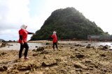 Wisatawan menikmati suasana di Pulau Merah, Banyuwangi, Jawa Timur, Jumat (7/12/2018). Pulau merah yang tercipta dari perjalanan magma dibawah gunung api purba itu, telah ditetapkan sebagai situs Geopark Nasional karena singkapan batuan yang membentuk pulau sangat ideal dijadikan labolatorium geologi dunia untuk mempelajari proses alterasi dan mineralisasi emas tembaga. Antara Jatim/Budi Candra Setya/ZK.