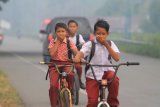 Sejumlah siswa naik sepeda sambil menutup hidung akibat kabut asap di Desa Suak Raya, Kecamatan Johan Pahlawan, Aceh Barat, Aceh, Rabu (30/1/2019). Kebakaran lahan gambut yang terjadi di kabupaten setempat menyebabkan jalan lintas diselimuti kabut asap dengan jarak pandang 30 - 70 meter. ANTARA FOTO/Syifa Yulinnas/nym.