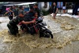 Prajurit TNI membantu seorang pengendara ketika berusaha menerobos banjir di Sentani, Jayapura, Papua, Kamis (21/3/2019). Hingga hari kelima pasca terjadinya banjir bandang, sejumlah ruas jalan utama masih terendam banjir dan sulit dilalui. ANTARA FOTO/Zabur Karuru/nym.