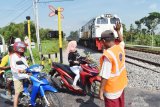 Relawan memberi isyarat kepada pengendara ketika ada Kereta Api (KA) melintas di perlintasan rel Kereta Api (KA) tanpa palang pintu di Kabupaten Madiun, Jawa Timur, Jumat (24/5/2019). Beberapa warga di sekitar perlintasan tersebut secara bergantian menjaga perlintasan rel KA tanpa palang pintu guna mengantisipasi terjadinya kecelakaan, dengan menerima imbalan dari pengendara secara sukarela. Antara Jatim/Siswowidodo/zk.