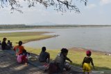 Pengunjung duduk di tepi Waduk Notopuro di Kabupaten Madiun, Jawa Timur, Minggu (30/6/2019). Waduk seluas 2.443 haktre tersebut airnya menyusut hingga sebagian dasar waduk mulai mengering. Antara Jatim/Siswowidodo/zk.