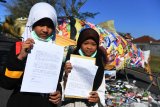 Dua anak pengunjuk rasa yang tegabung dalam Brantas River Coalition to Stop Imported Plastic Trash (BRICSIP)   menunjukan surat yang akan dikirim kepada Presiden Amerika Serikat Donald Trump saat aksi Jawa Timur bukan tempat sampah Amerika Serikat di depan Kantor Konsulat Jenderal Amerika Serikat di Surabaya, Jawa Timur,  Jumat (12/7/2019). Dalam aksinya mereka menyerukan agar Pemerintah Amerika Serikat menghentikan penyelundupan sampah rumah tangga ke dalam kertas yang diekspor ke Indonesia khususnya Jawa Timur.  Antara Jatim/Zabur Karuru