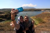 Pengunjung berswafoto dengan latar belakang Waduk Bajulmati, Banyuwangi, Jawa Timur, Rabu (31/7/2019). Waduk yang mampu menampung air sekitar 10 juta meterkubik tersebut pada musim kemarau mengalami penurunan volume air namun diharapkan dapat mensuplai kebutuhan air untuk pertanian di wilayah itu.  Antara Jatim/Budi Candra Setya/zk