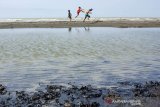 Sejumlah anak bermain di sekitar pantai terdampak tumpahan minyak mentah yang tercecer di Pesisir Pantai Tanjungsari, Karawang, Jawa Barat, Kamis (8/8/2019). PT. Pertamina mengklaim volume tumpahan minyak mentah yang tercecer akibat kebocoran gas di anjungan lepas pantai YY PHE ONWJ di wilayah Karawang tinggal 10 persen dibandingkan dari volume awal yang ditaksir mencapai 3.000 barel per hari. ANTARA JABAR/M Ibnu Chazar/agr