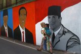 Seorang ibu yang menggendong anaknya melintas di depan mural Presiden Joko Widodo, mantan Presiden Soekarno dan Susilo Bambang Yudhoyono di Sukun, Malang, Jawa Timur, Senin (12/8/2019). Mural presiden dan mantan presiden tersebut sengaja di gambar warga setempat untuk menyambut HUT Kemerdekaan RI Ke-74. Antara Jatim/Ari Bowo Sucipto/zk.