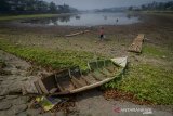 Warga melintas di pinggir perahu yang karam di tepi Situ Ciburuy yang menyusut di Padalarang, Kabupaten Bandung Barat, Jawa Barat, Kamis (19/9/2019). Kemarau panjang yang telah berlangsung selama beberapa bulan di Jawa Barat membuat debit air Situ Ciburuy menurun hingga lima meter dan menyisakan kedalaman hanya satu meter. ANTARA FOTO/Raisan Al Farisi/agr